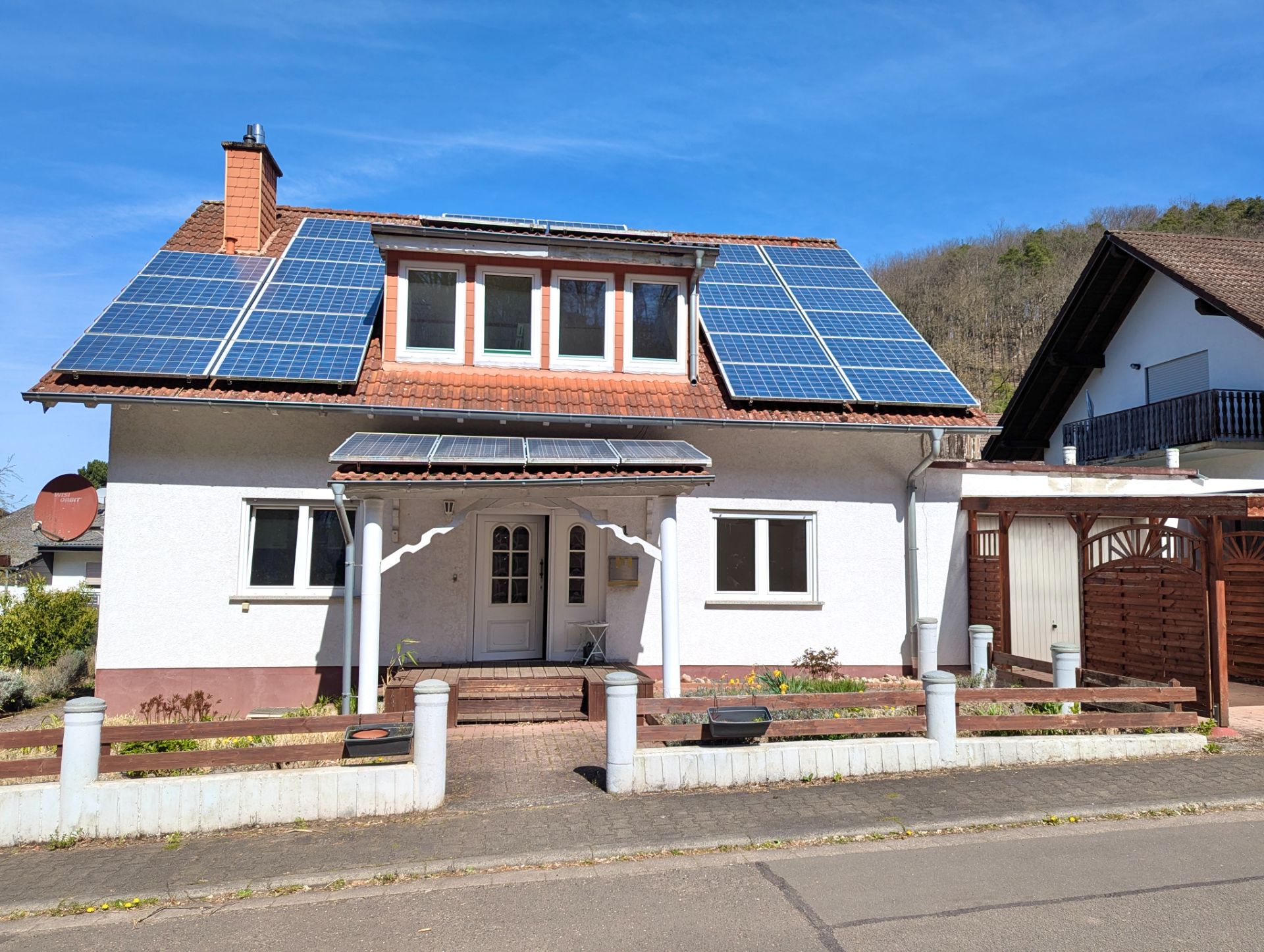 Weißes Wohnhaus mit Solarpanels auf dem Dach, Vorgarten und Garage rechts.