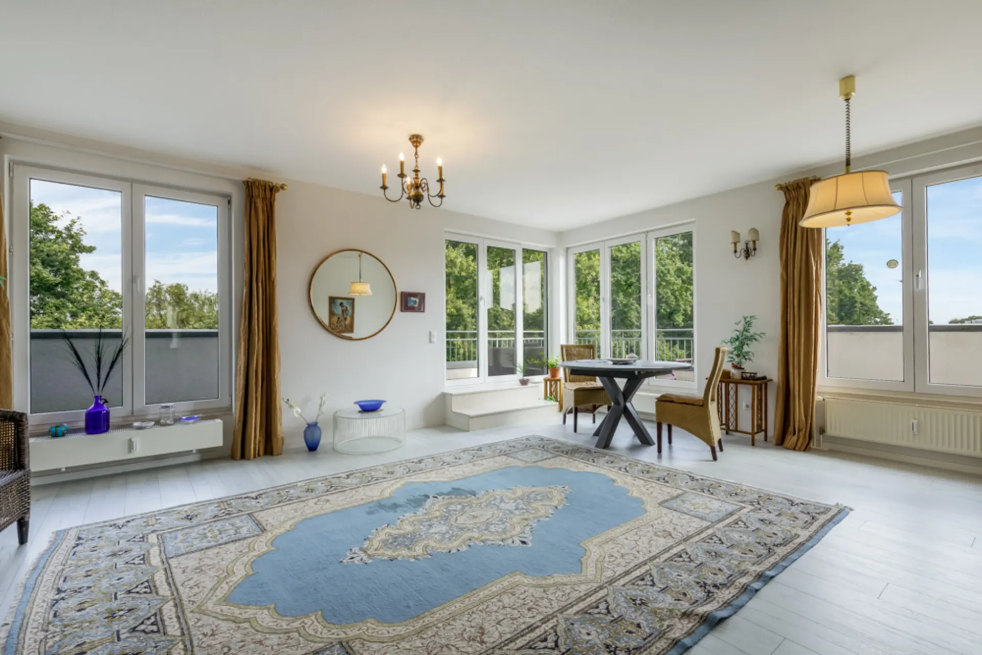 Helles Wohnzimmer mit großen Fenstern, Esstisch und Teppich, Blick ins Grüne.