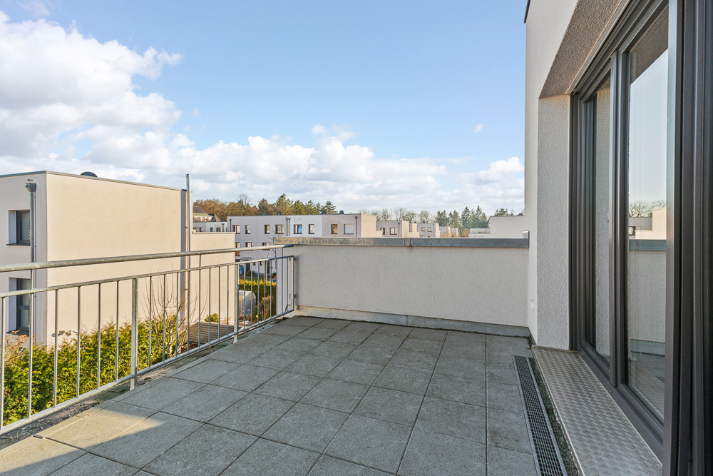 Geräumiger Balkon mit Fliesenboden und Metallgeländer, Blick auf moderne Wohngebäude.
