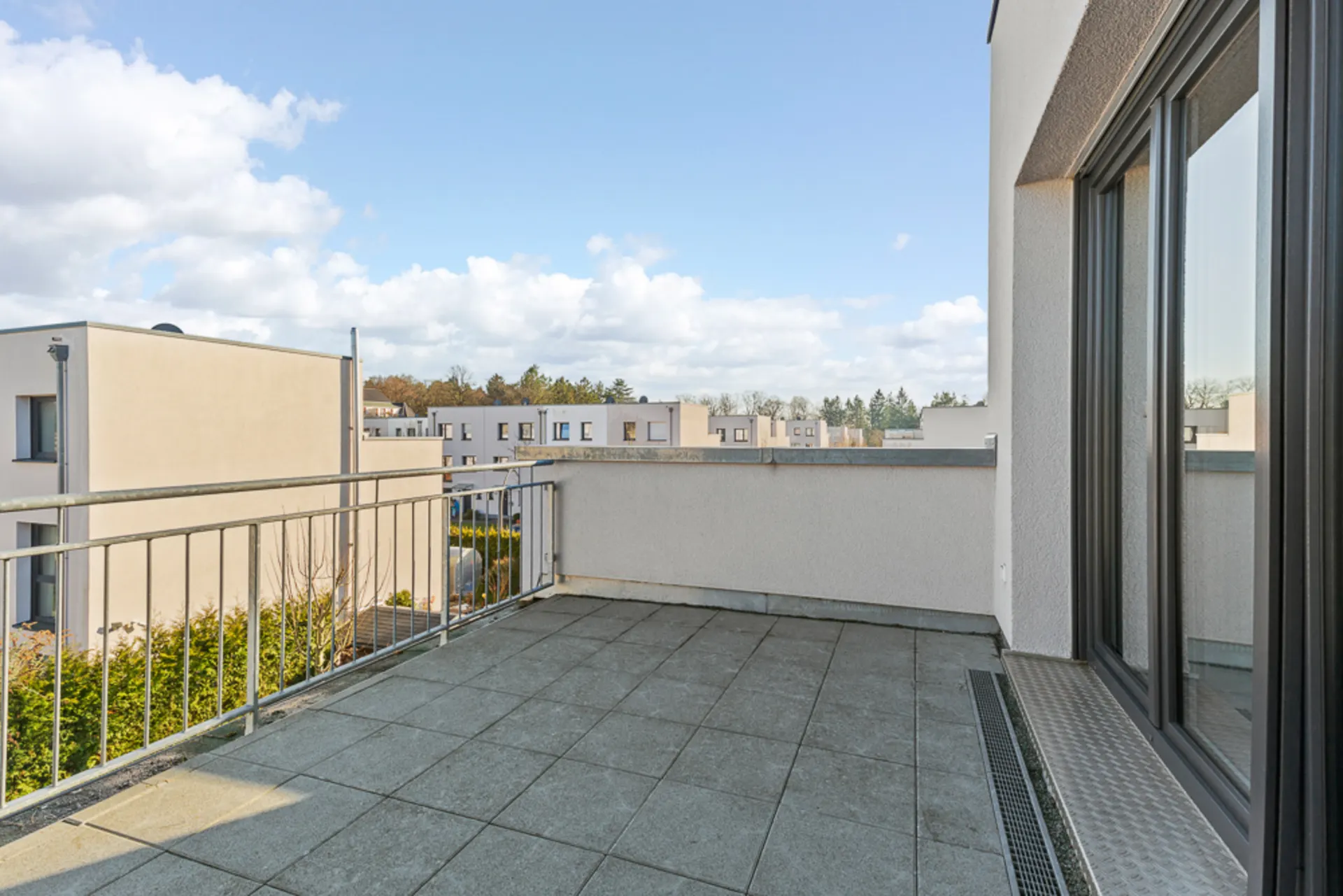 Geräumiger Balkon mit Fliesenboden und Metallgeländer, Blick auf moderne Wohngebäude.