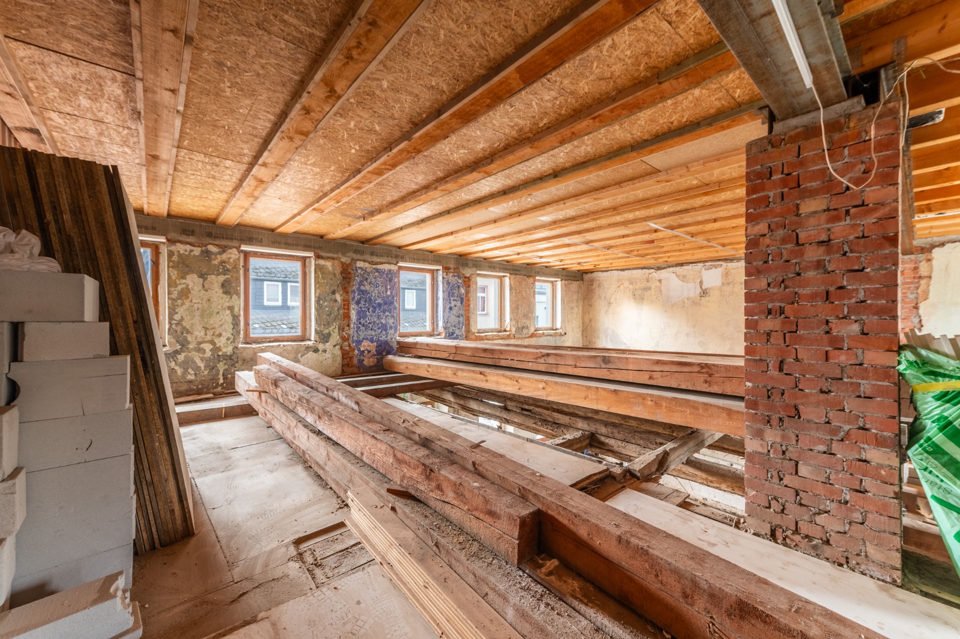Dachboden mit Holzbalken, offenen Wänden und mehreren Fenstern, im Renovierungszustand.
