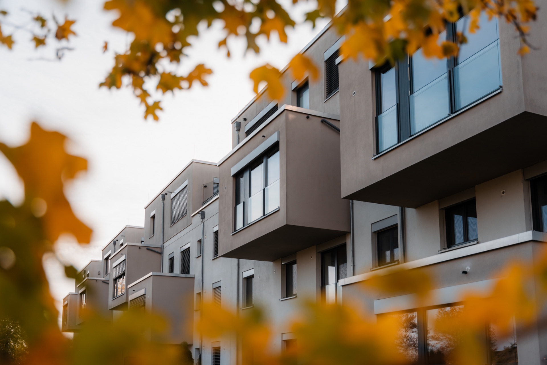 Moderne Wohngebäude mit Balkonen, umrahmt von gelben Herbstblättern.