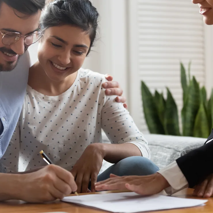 Ein Paar sitzt auf dem Sofa und unterschreibt gemeinsam ein Dokument am Tisch.