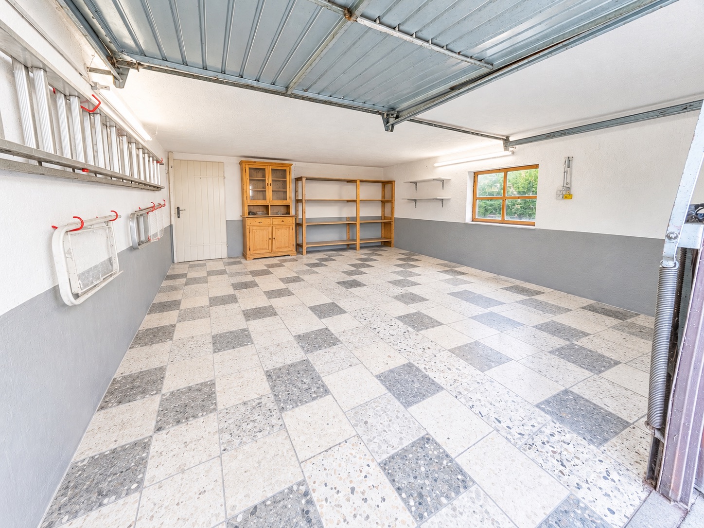Leere Garage mit kariertem Boden, Regalen und Leitern an der Wand.