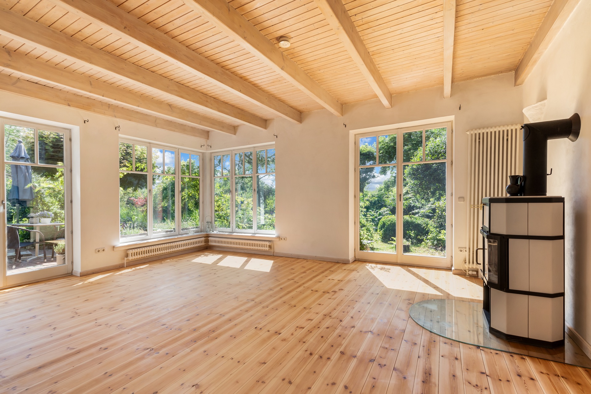 Helles Wohnzimmer mit Holzboden, großen Fenstern und Kaminofen.