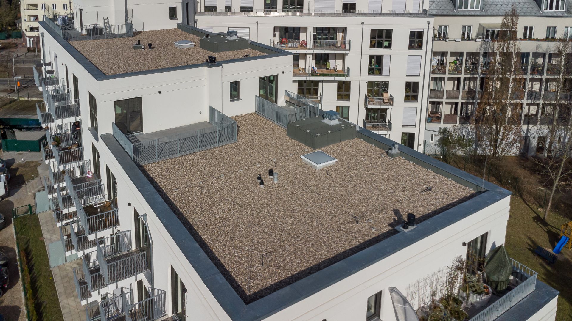 Dach eines modernen Wohngebäudes mit Kies und mehreren Balkonen an der Fassade.