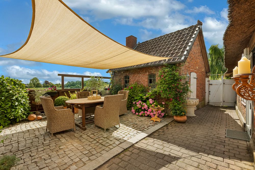 Gemütliche Terrasse mit Esstisch, Stühlen, Pflanzen und Sonnensegel neben Backsteinhaus.