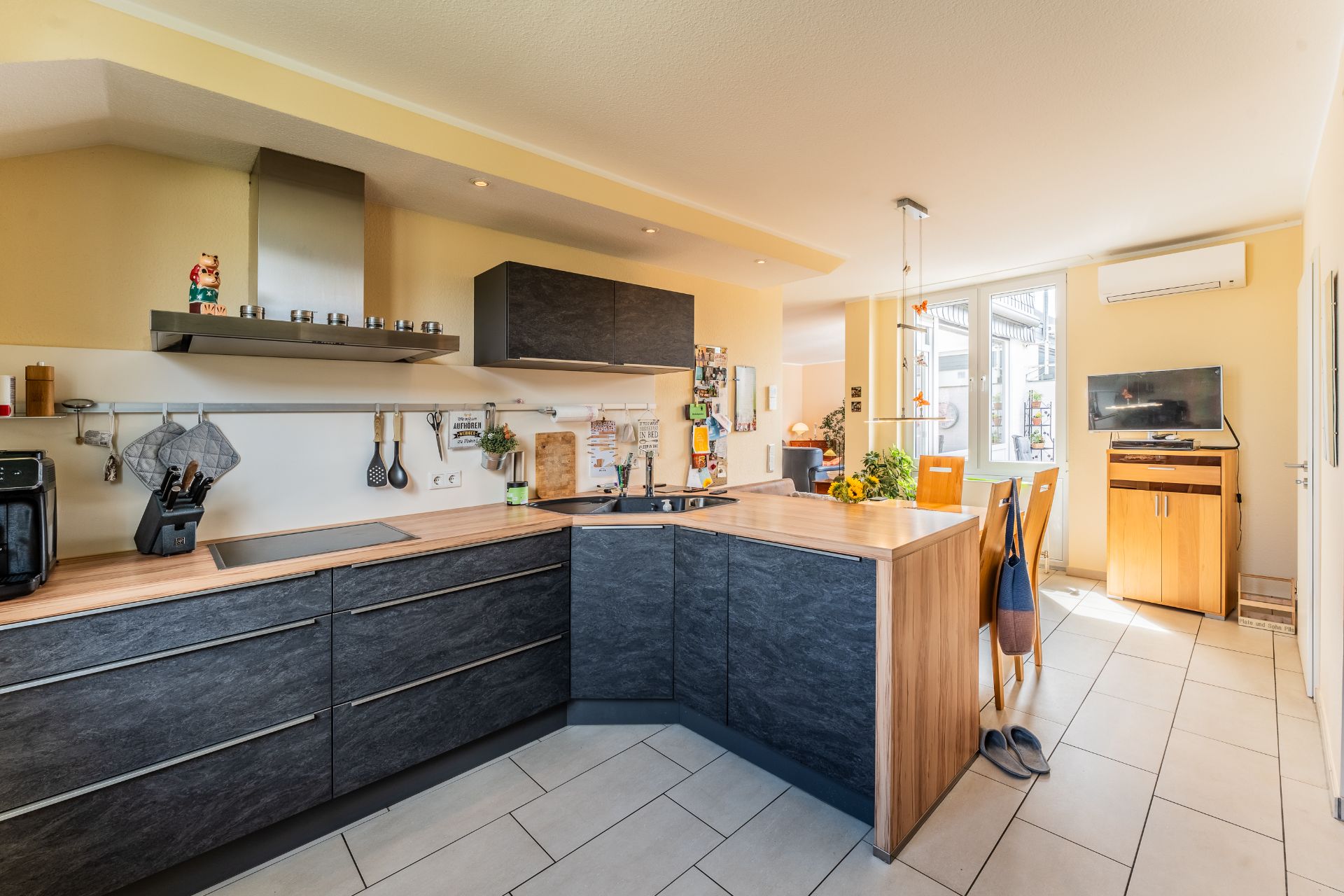 Moderne Einbauküche mit Holztisch, Essbereich, Fernseher und großen Fenstern.