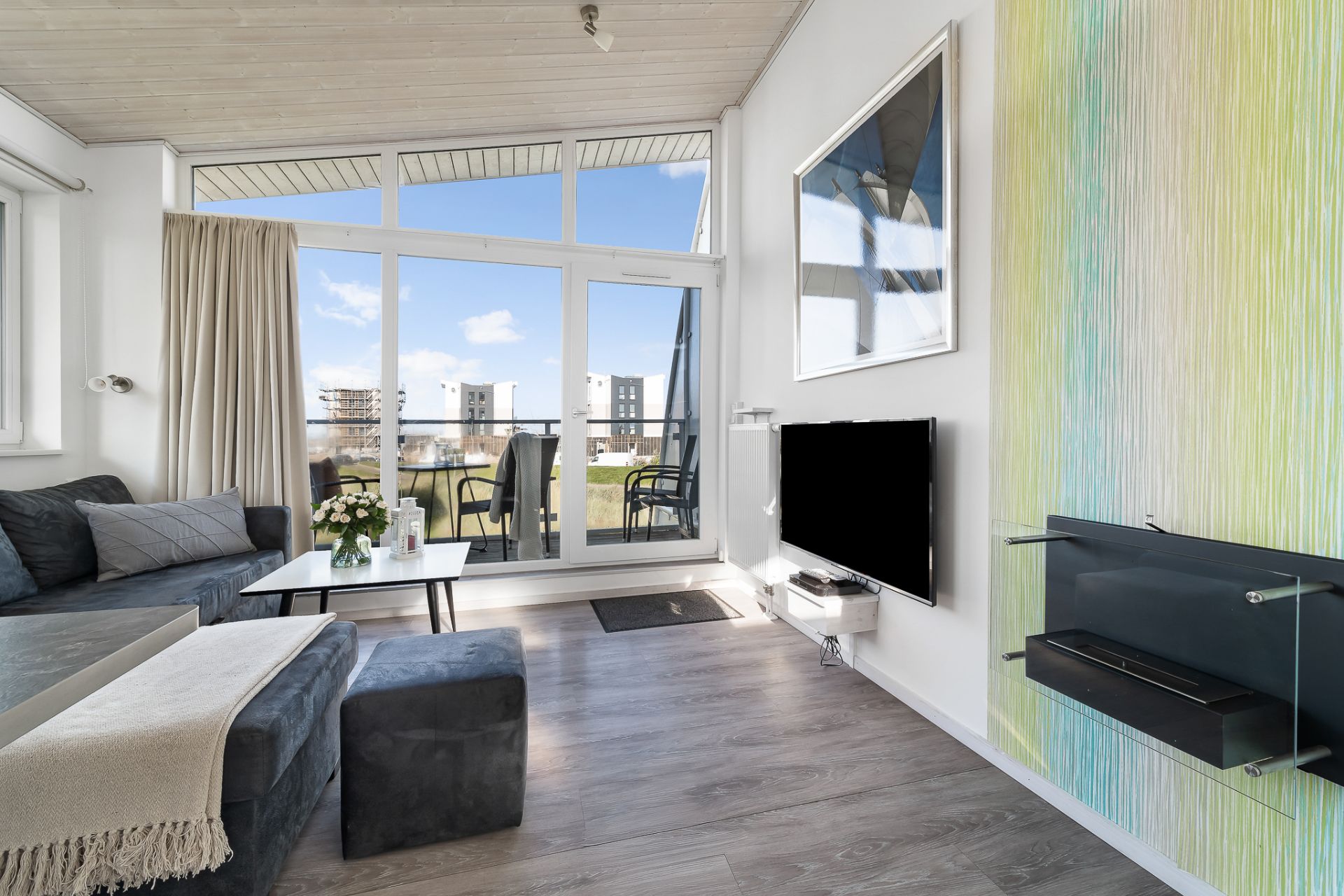 Wohnzimmer mit Sofa, Couchtisch, Fernseher und großem Fenster zur Terrasse.