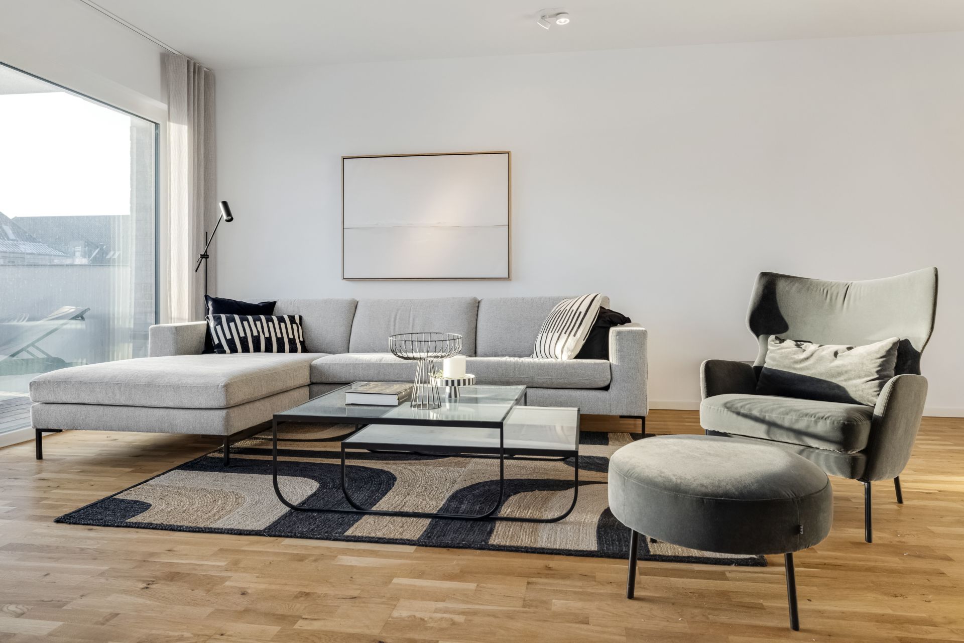 Modernes Wohnzimmer mit grauem Sofa, Sessel, Couchtisch und großem Fenster.