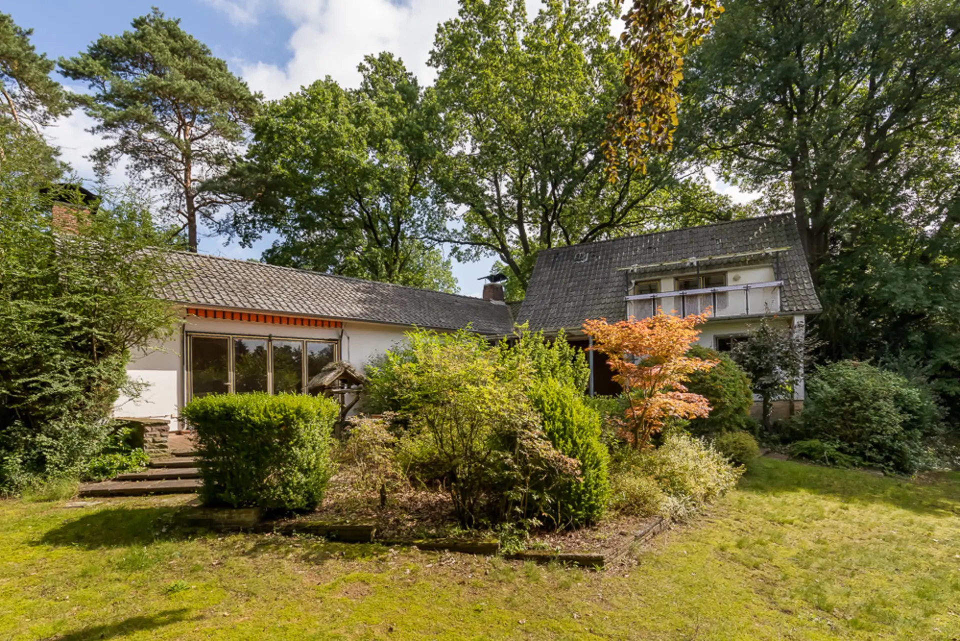 Haus mit großem Garten, vielen Bäumen und Sträuchern an einem sonnigen Tag.