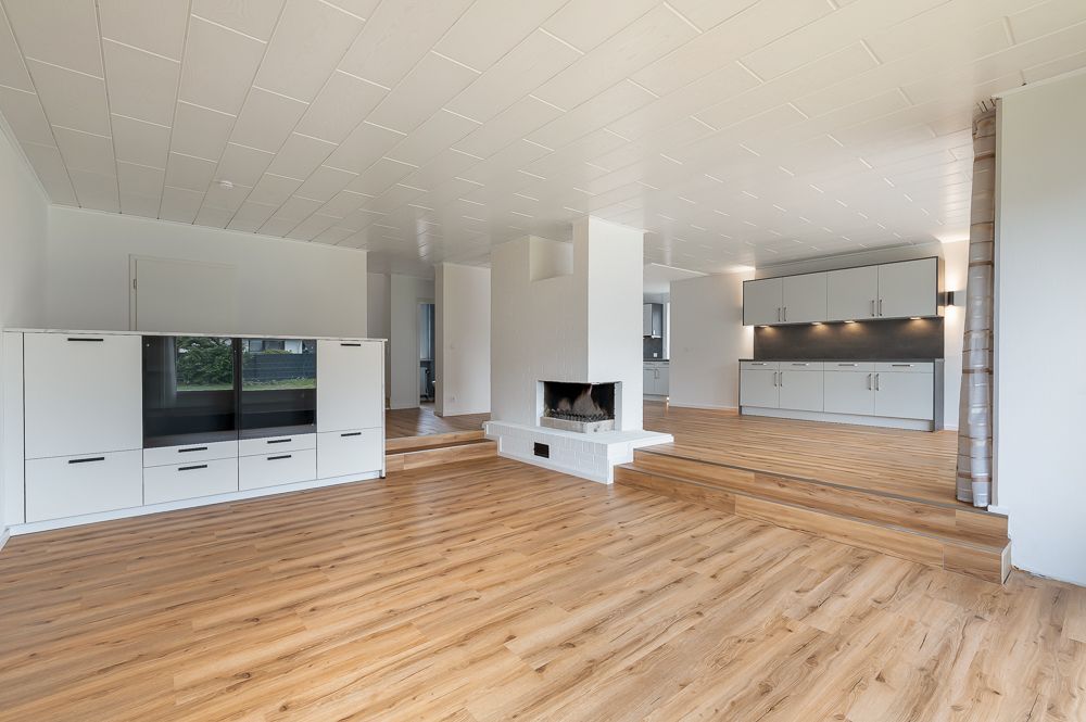 Helles Wohnzimmer mit Holzfußboden, Kamin, Einbauschränken und offener Küche.