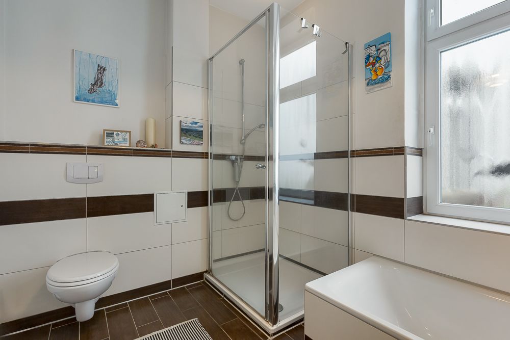 Modernes Bad mit Dusche, Badewanne, WC und Fenster, weiße Fliesen mit braunen Akzenten.