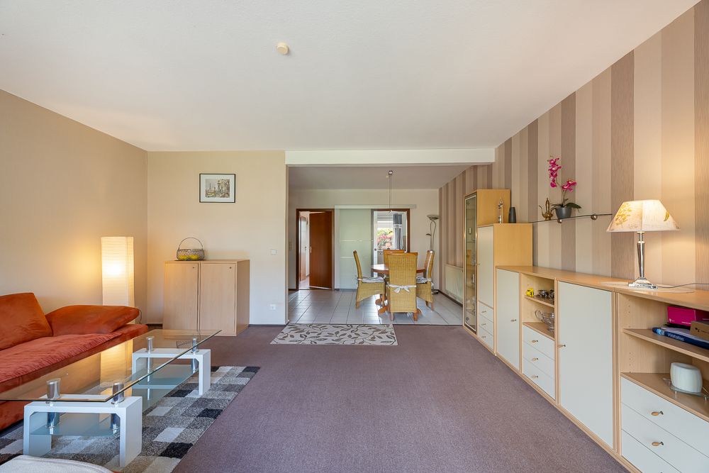 Wohnzimmer mit rotem Sofa, Glastisch, Teppich und Blick auf Essbereich mit Holzmöbeln.