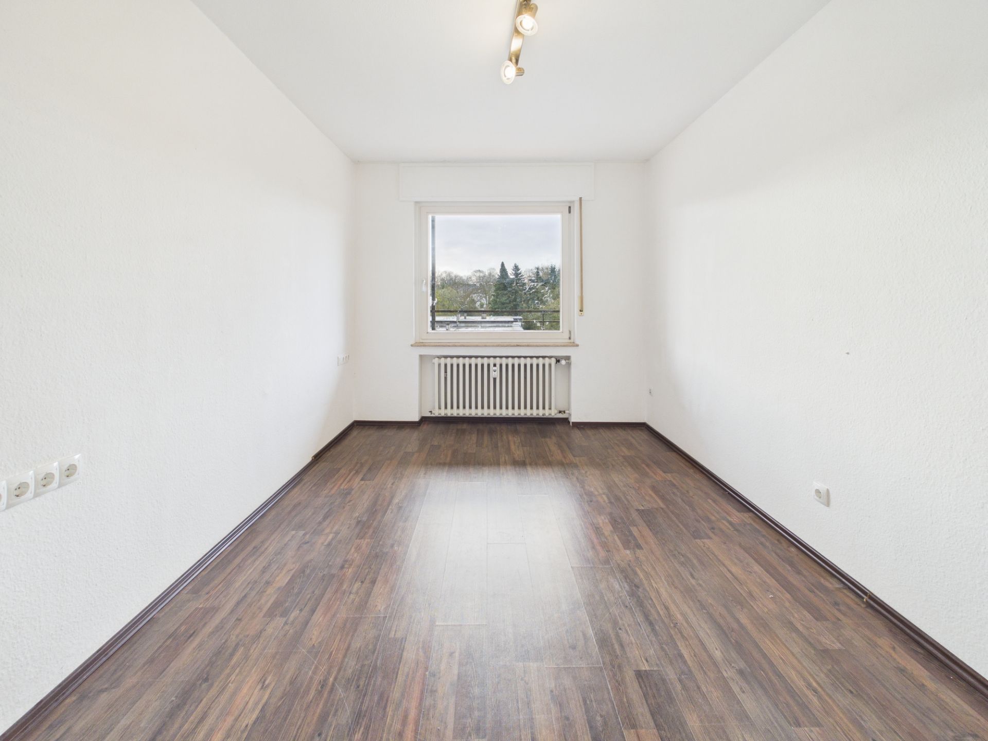 Leerer, heller Raum mit Holzfußboden, weiß gestrichenen Wänden und Fenster mit Ausblick.