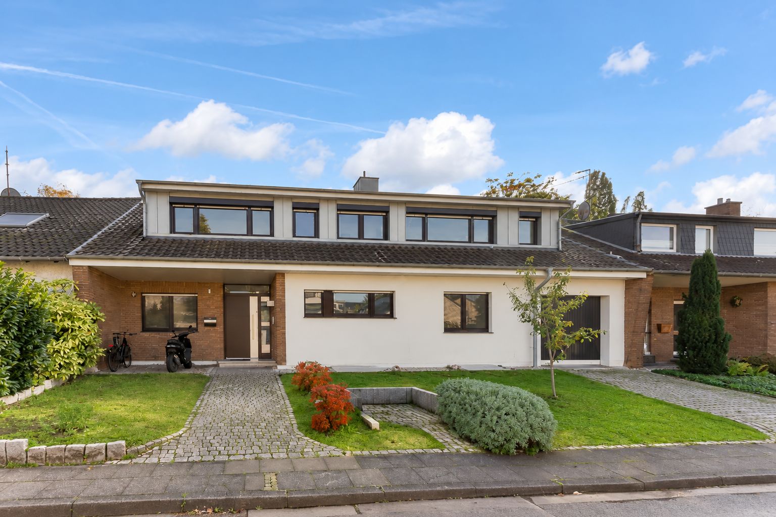 Einfamilienhaus mit flachem Dach, Vorgarten, Bäumen und gepflastertem Weg zum Eingang.