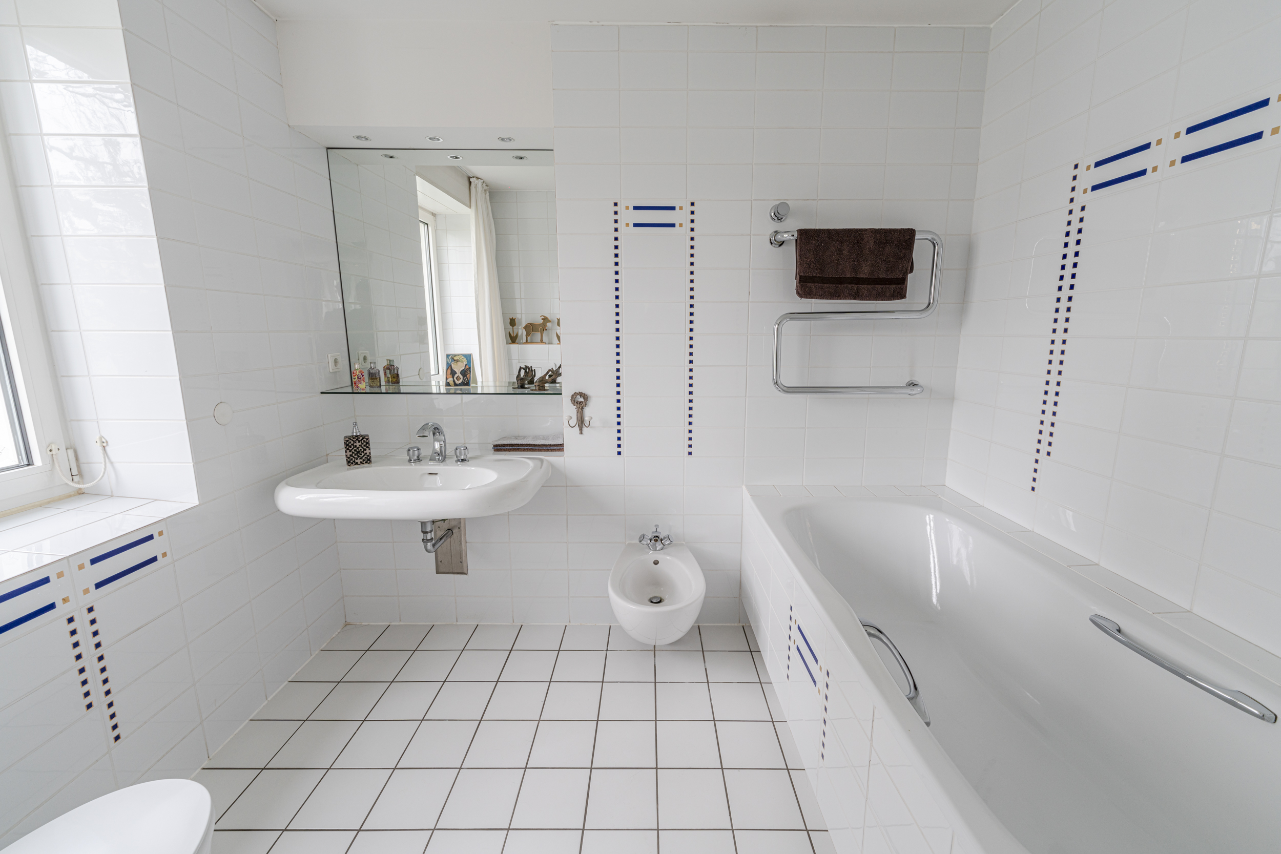 Helles Badezimmer mit Badewanne, Waschbecken, Bidet, großem Spiegel und weißen Fliesen.