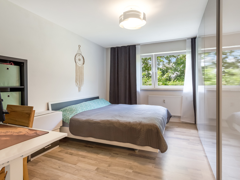 Modernes Schlafzimmer mit Doppelbett, großem Fenster, Vorhängen und Kleiderschrank auf Holzfußboden.