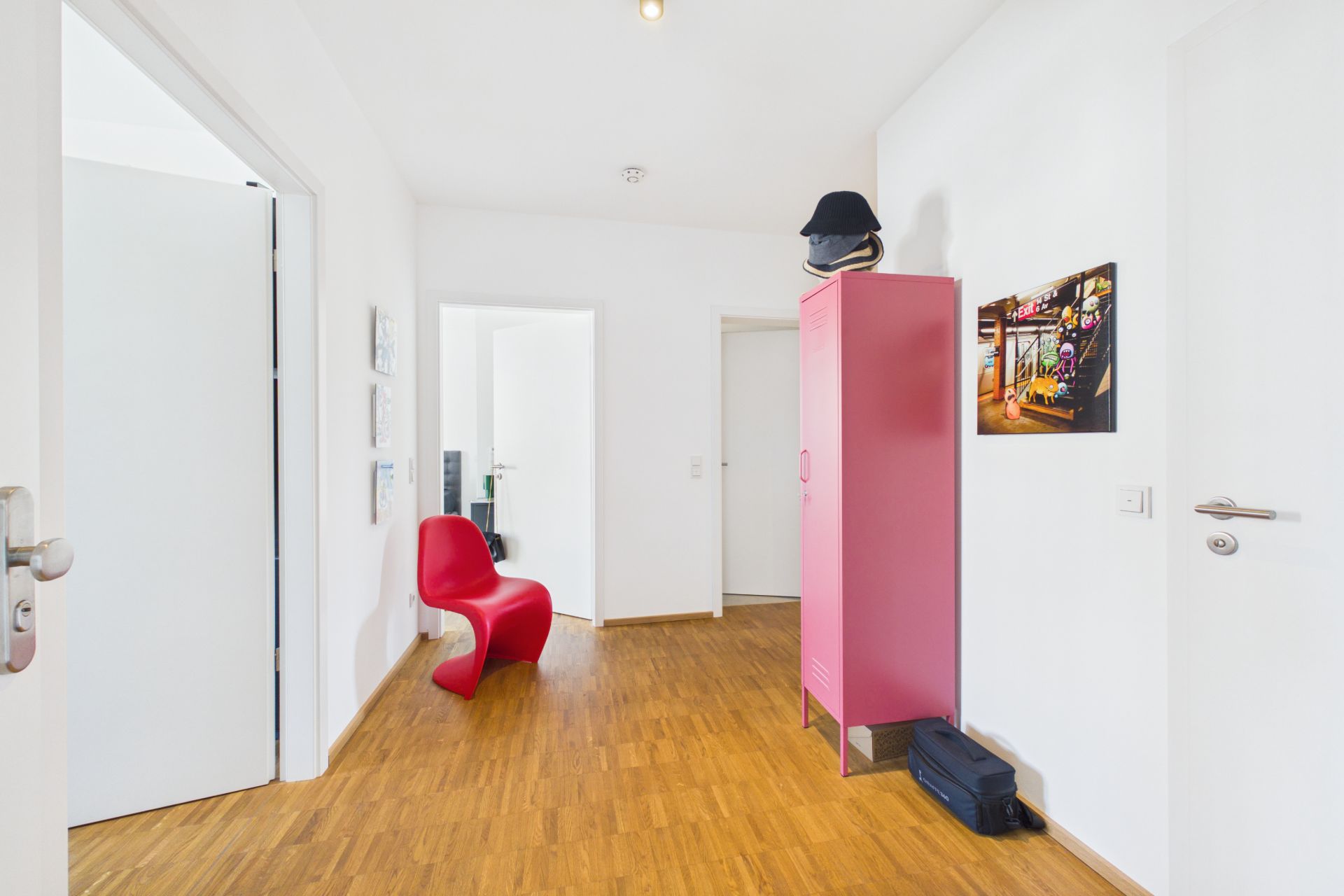 Heller Flur mit rotem Stuhl, pinkem Schrank und Holzfußboden.