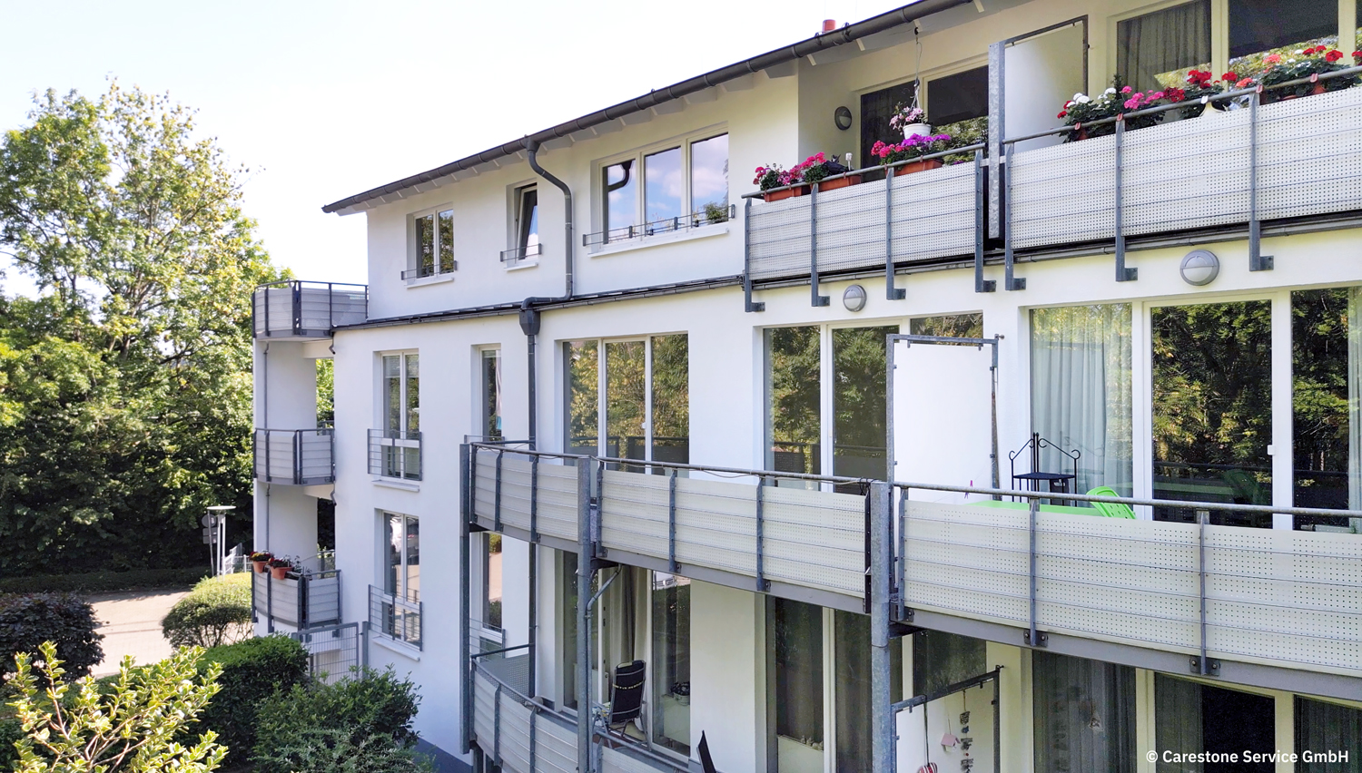 Mehrfamilienhaus mit weißen Fassaden und mehreren Balkonen, umgeben von Bäumen.
