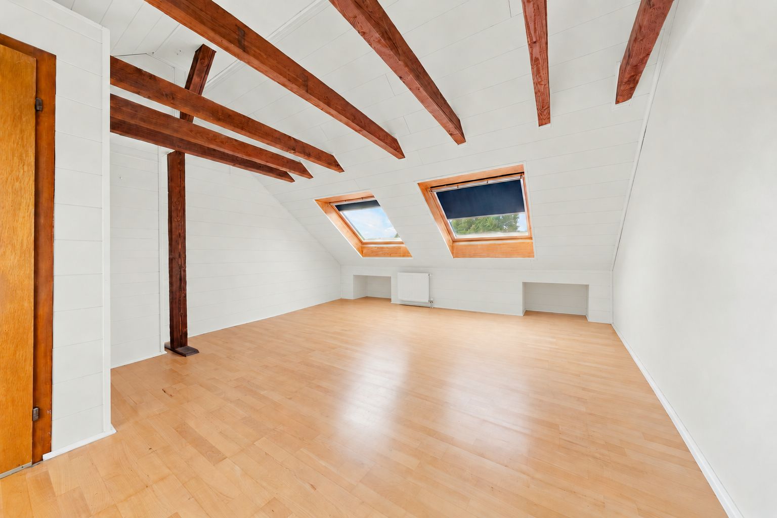 Heller Dachbodenraum mit Holzbalken, zwei Dachfenstern und hellem Laminatboden.