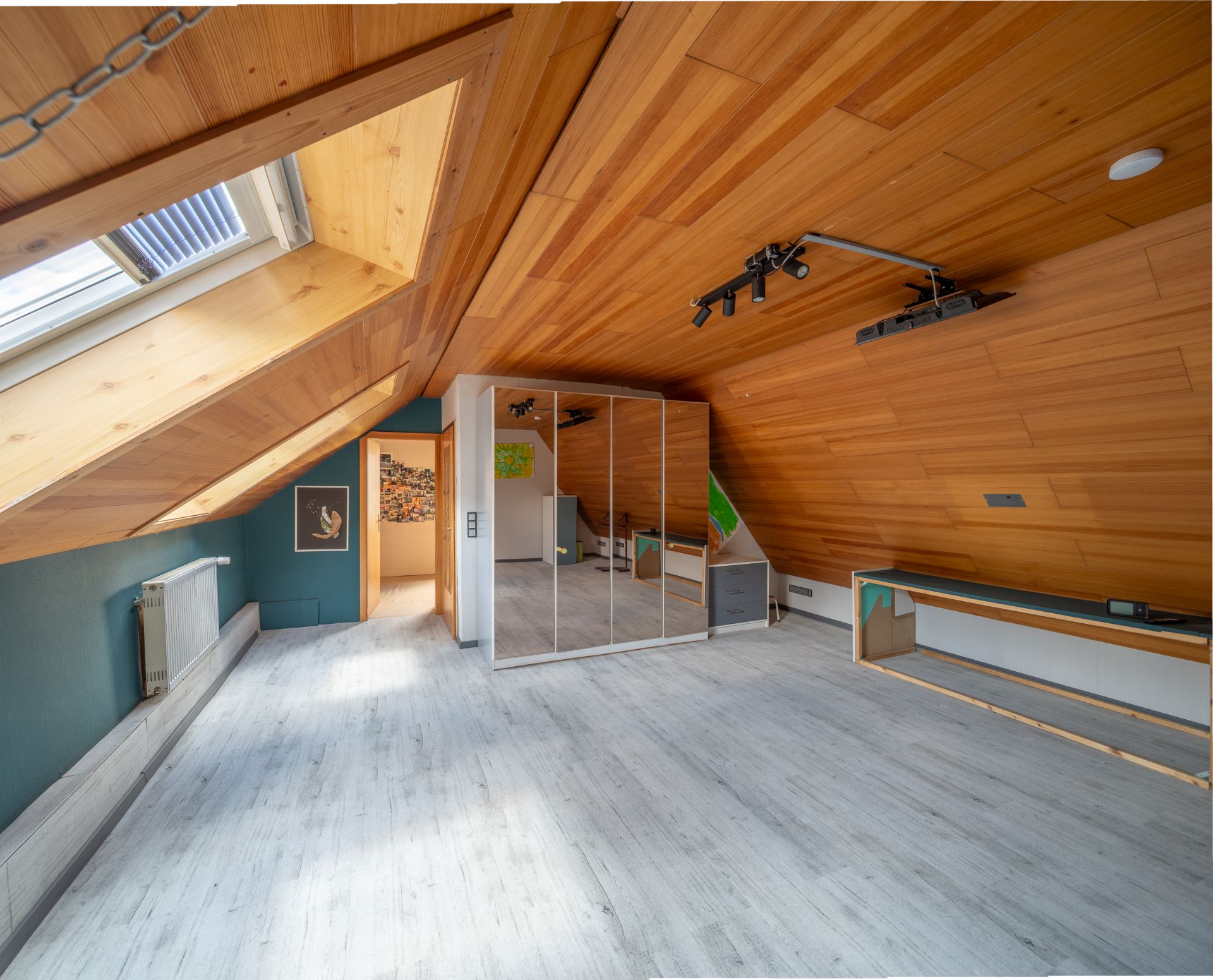 Dachzimmer mit Holzdecke, Dachfenster, Spiegel-Schrank und hellem Boden.