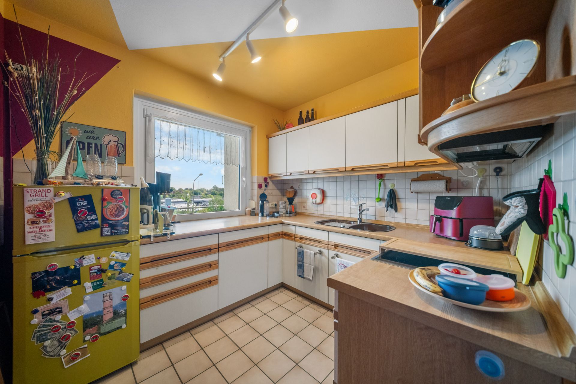 Helle Küche mit gelben Wänden, weißen Schränken, gelbem Kühlschrank und Fenster mit Blick nach draußen.