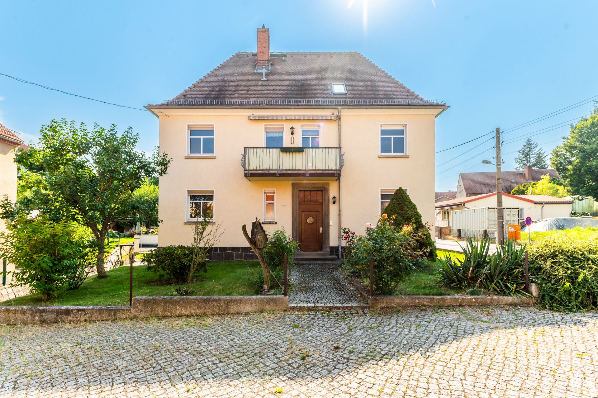 Zweistöckiges Haus mit Garten, Balkon und gepflastertem Weg im Vordergrund.