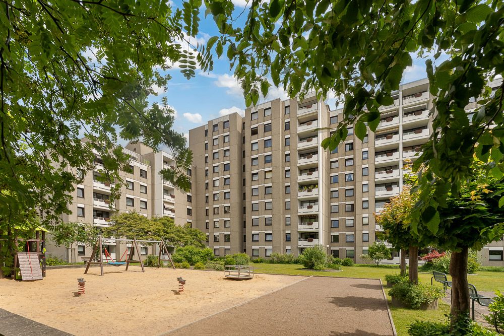 Mehrstöckige Wohngebäude mit kleinem Spielplatz und Bäumen im Vordergrund.