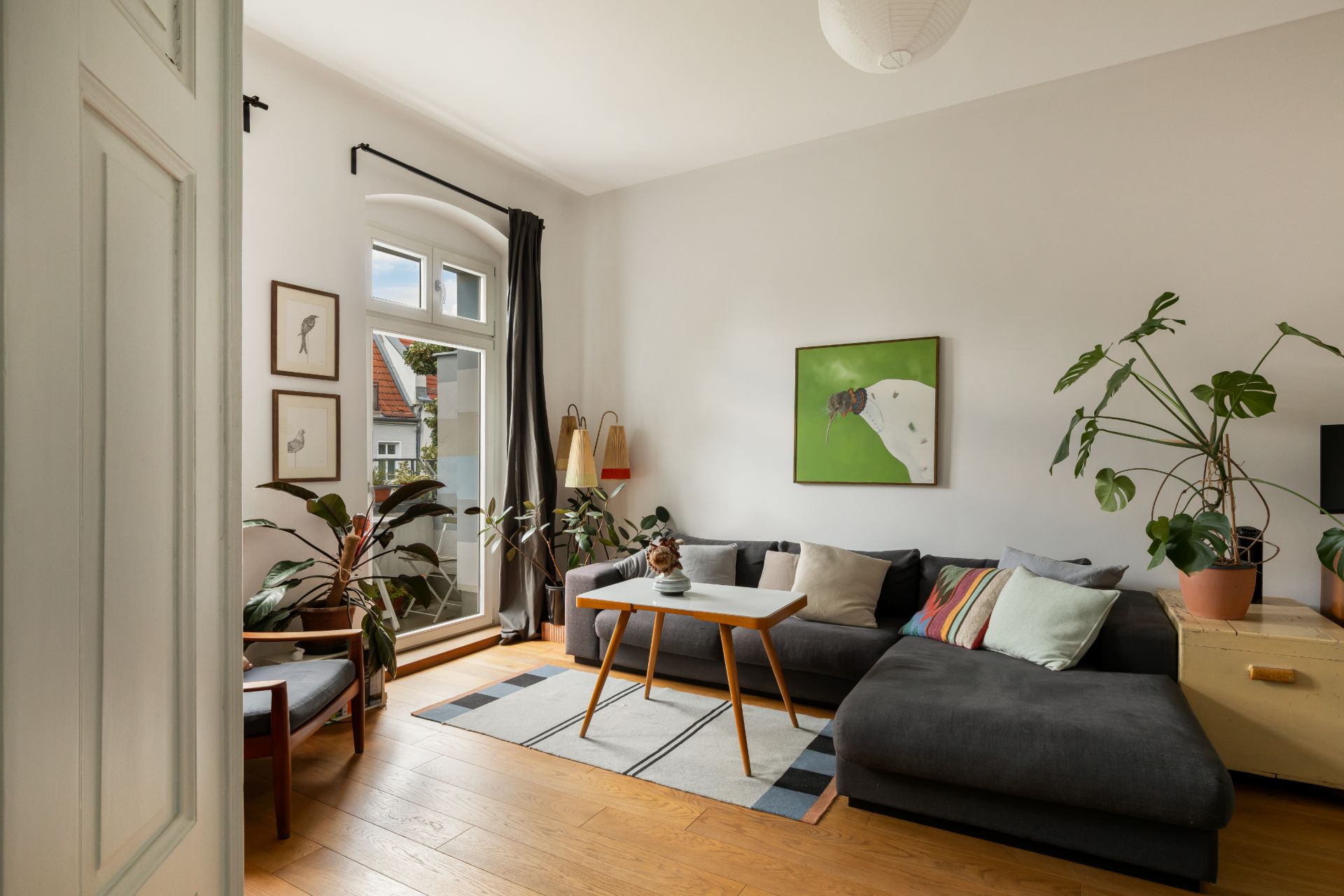 Helles Wohnzimmer mit Ecksofa, Holztisch, Pflanzen und Bildern an der Wand.