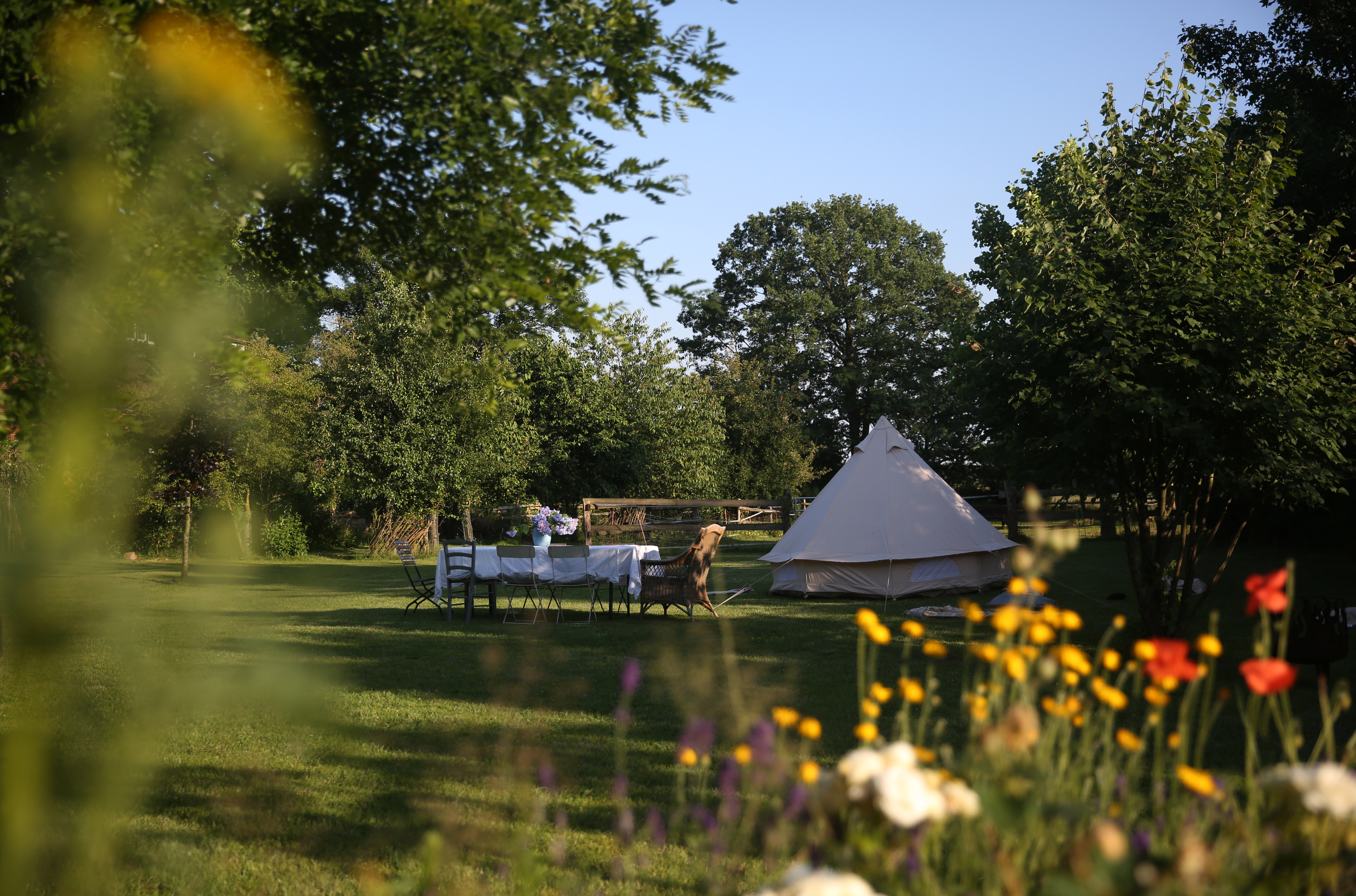 Großer Garten mit Esstisch, Stühlen und einem Zelt, umgeben von Bäumen und Blumen.