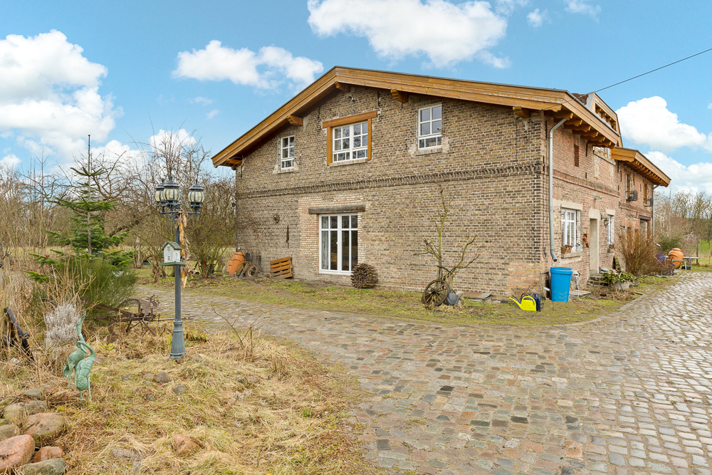 Backsteinhaus mit Satteldach und Kopfsteinpflasterweg, umgeben von Garten und Dekorationen.