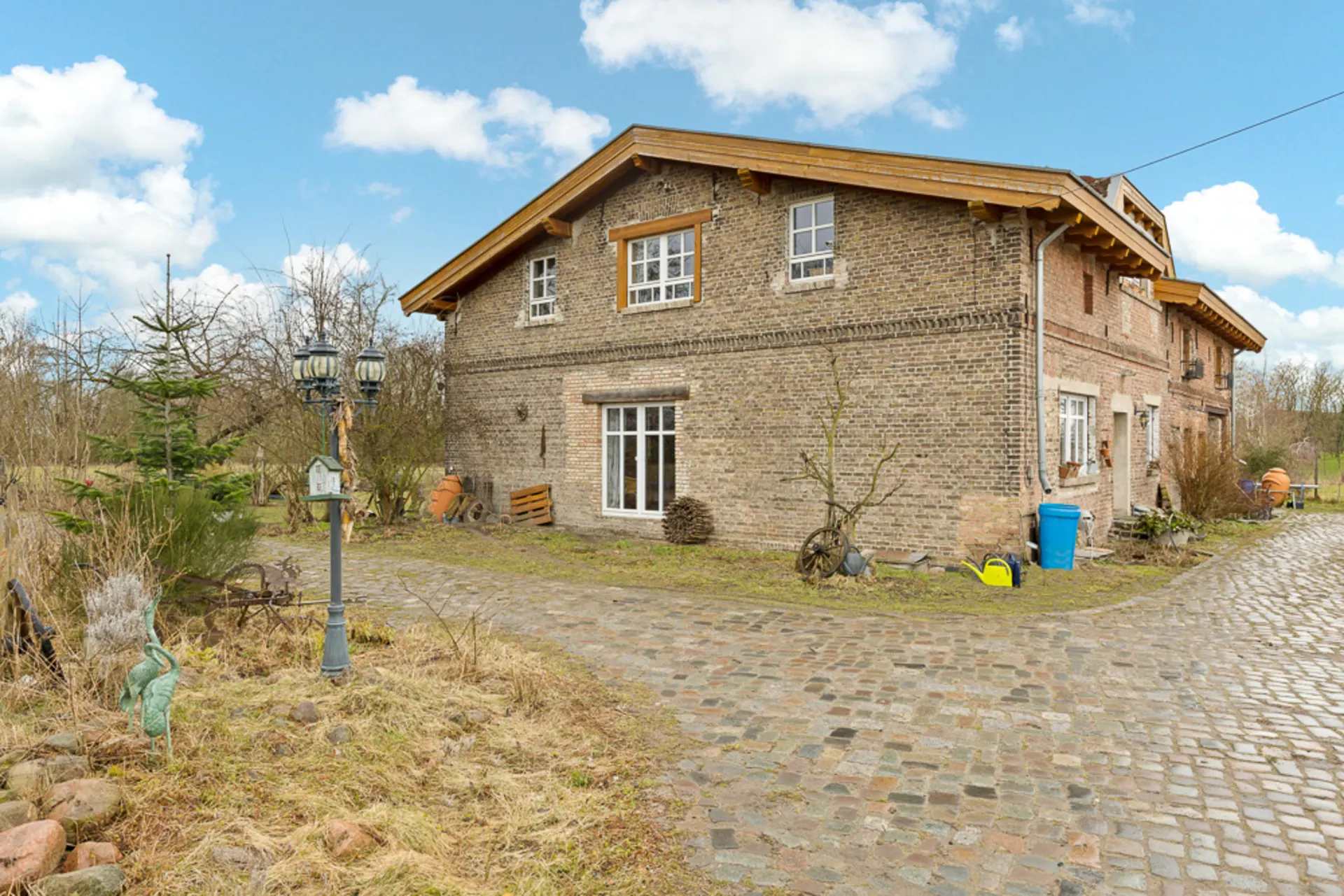 Backsteinhaus mit Satteldach und Kopfsteinpflasterweg, umgeben von Garten und Dekorationen.