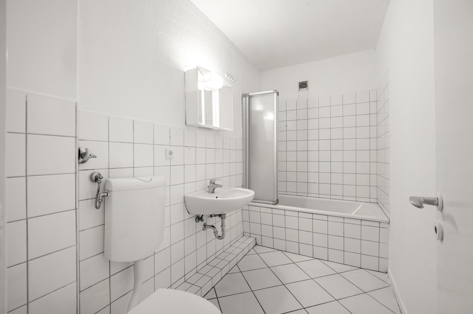 Helles Badezimmer mit weiß gefliesten Wänden, WC, Waschbecken, Badewanne und Spiegel.