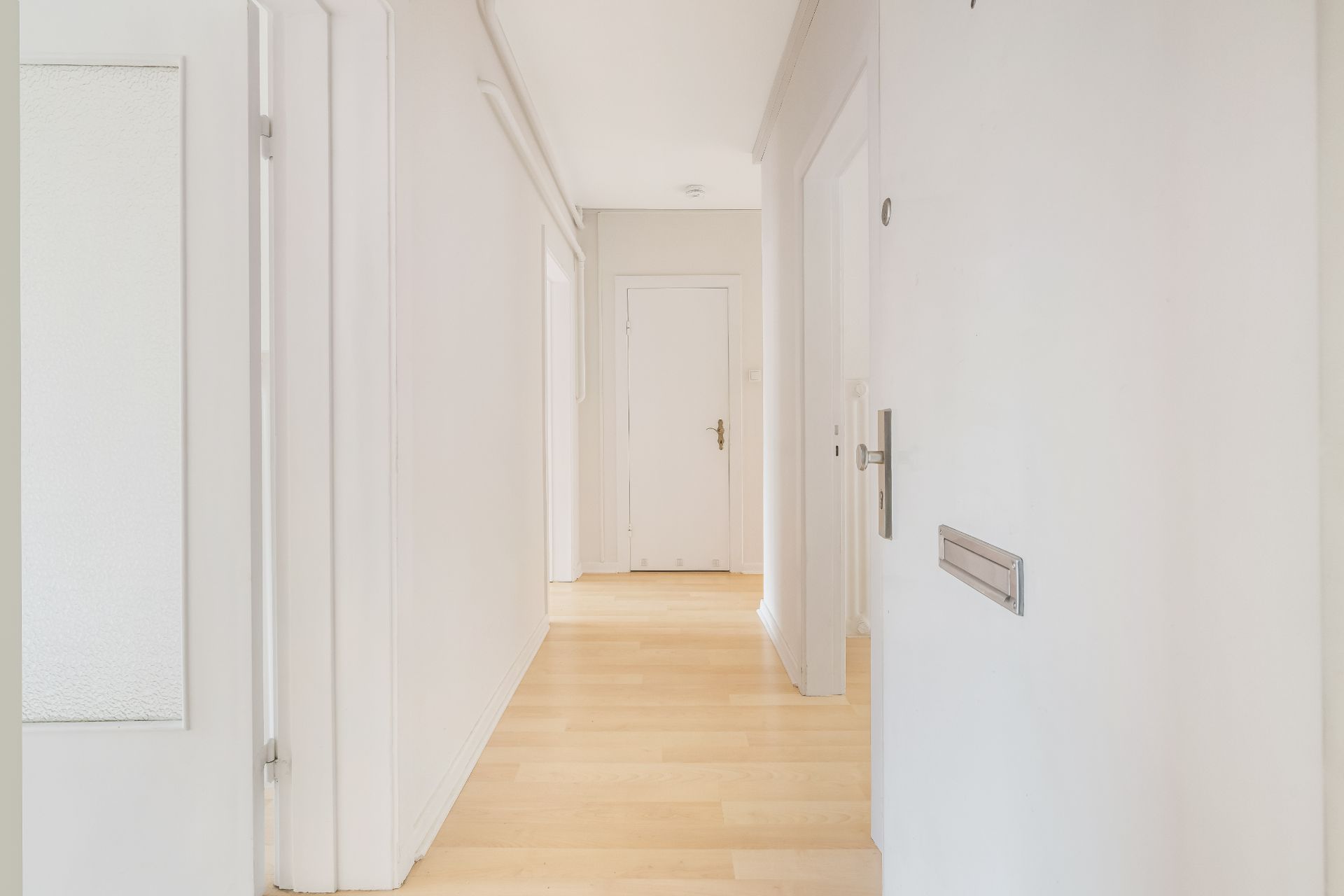 Heller Flur mit Holzboden und weißen Wänden, mehrere Türen führen in verschiedene Räume.