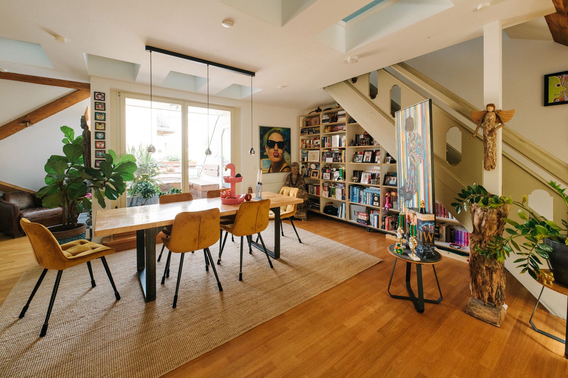Helles Esszimmer mit Holztisch, gelben Stühlen, Bücherregalen und Pflanzen.