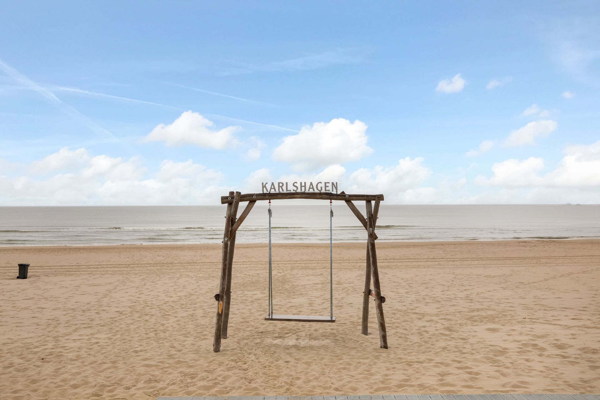 Holzschaukel mit Schild 'Karlshagen' am Sandstrand vor dem Meer.