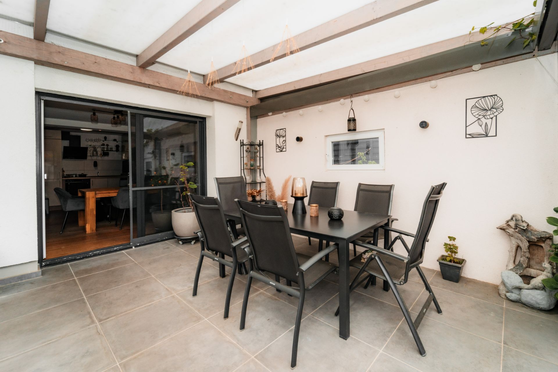 Überdachte Terrasse mit Esstisch und acht Stühlen, Wanddekorationen und Pflanzen.