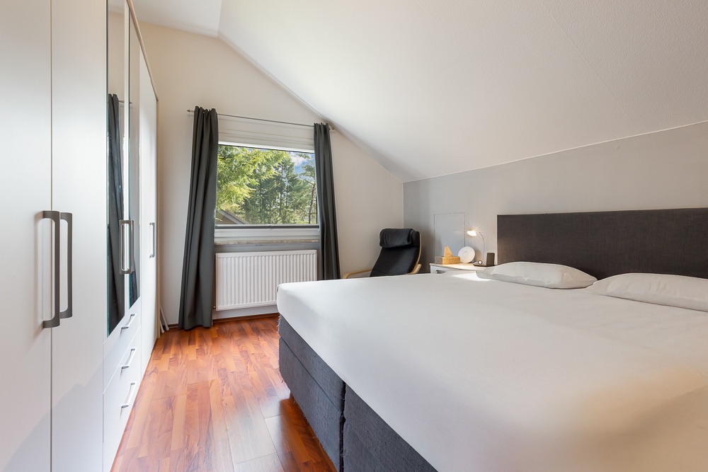 Modernes Schlafzimmer mit Doppelbett, weißem Kleiderschrank und Fenster mit Blick ins Grüne.