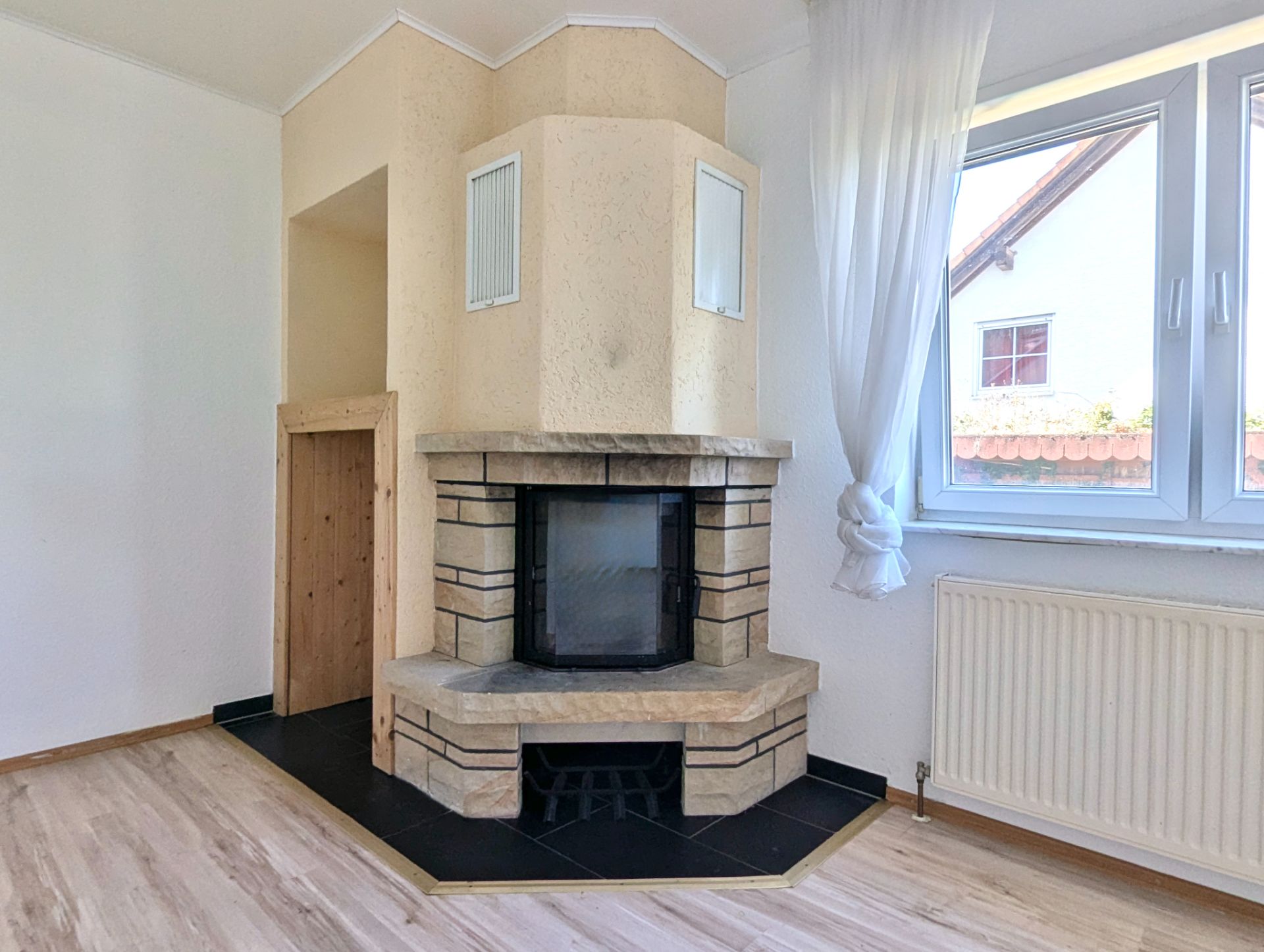 Wohnzimmer mit Kamin, großen Fenstern und hellen Vorhängen.