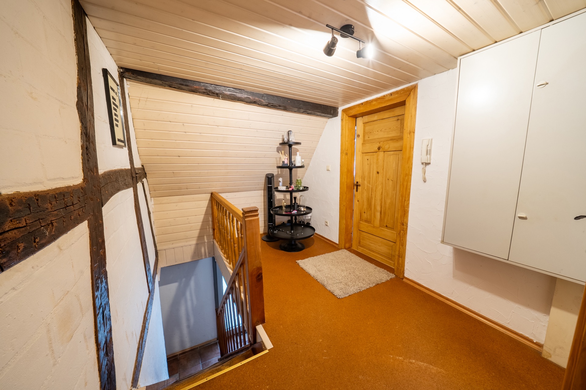 Flur mit Holztreppe, Holztür, Regal, weißer Decke und Wandschrank.