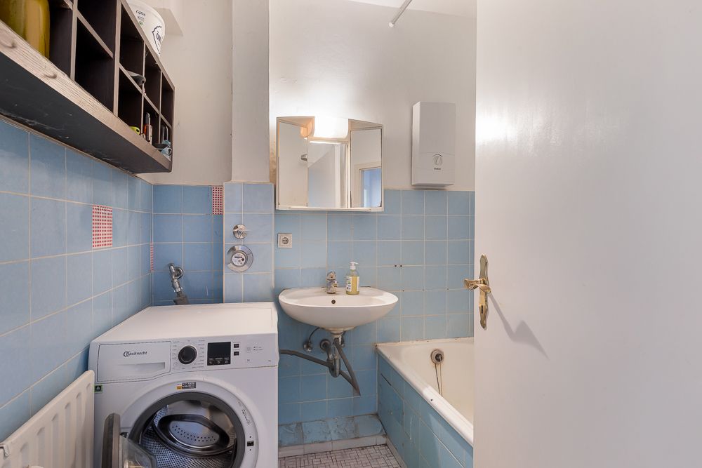 Kleines Badezimmer mit blauen Fliesen, Waschmaschine, Waschbecken und Badewanne.