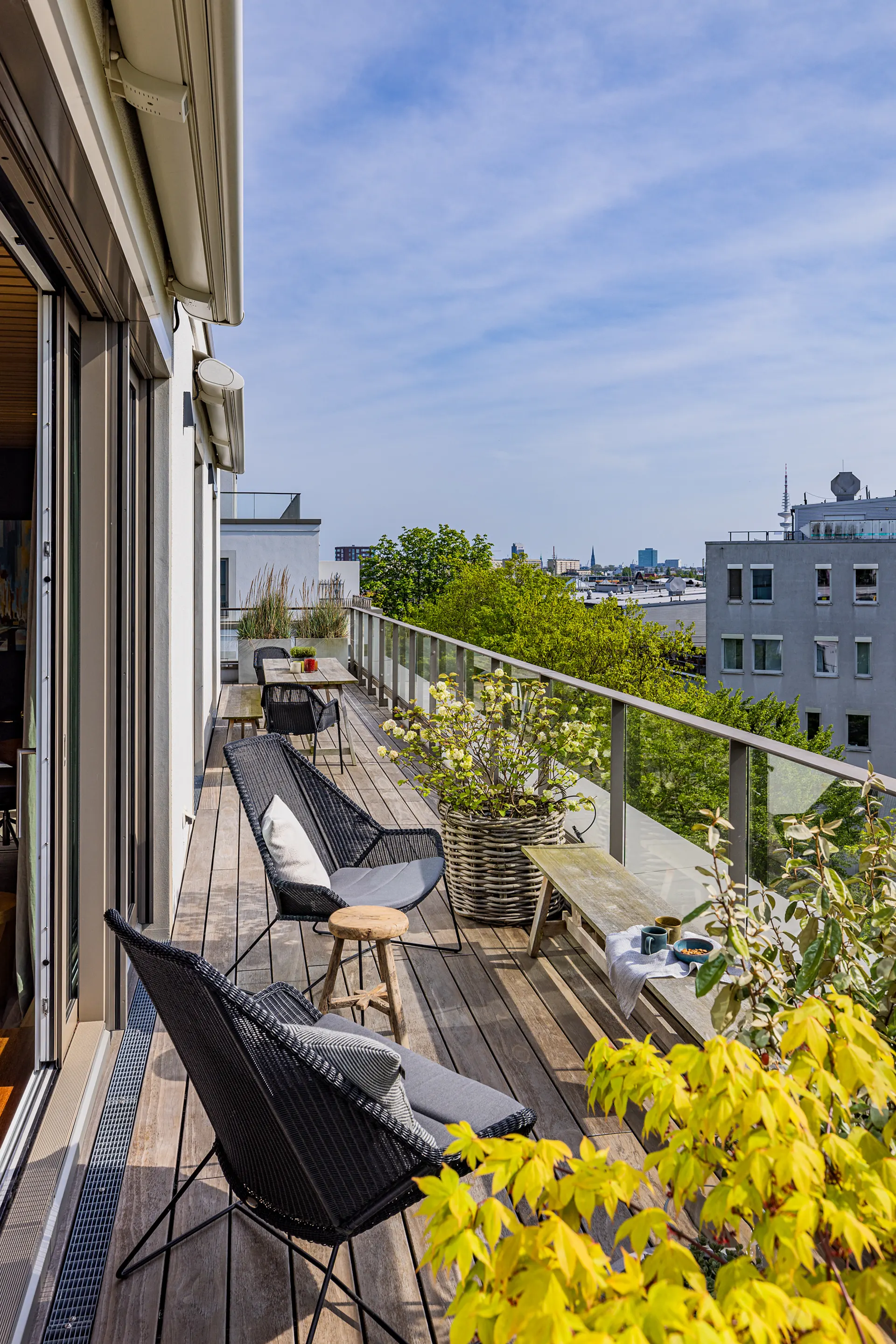 Holzterrasse mit Stühlen, Pflanzen und Blick auf eine Stadt im Hintergrund.