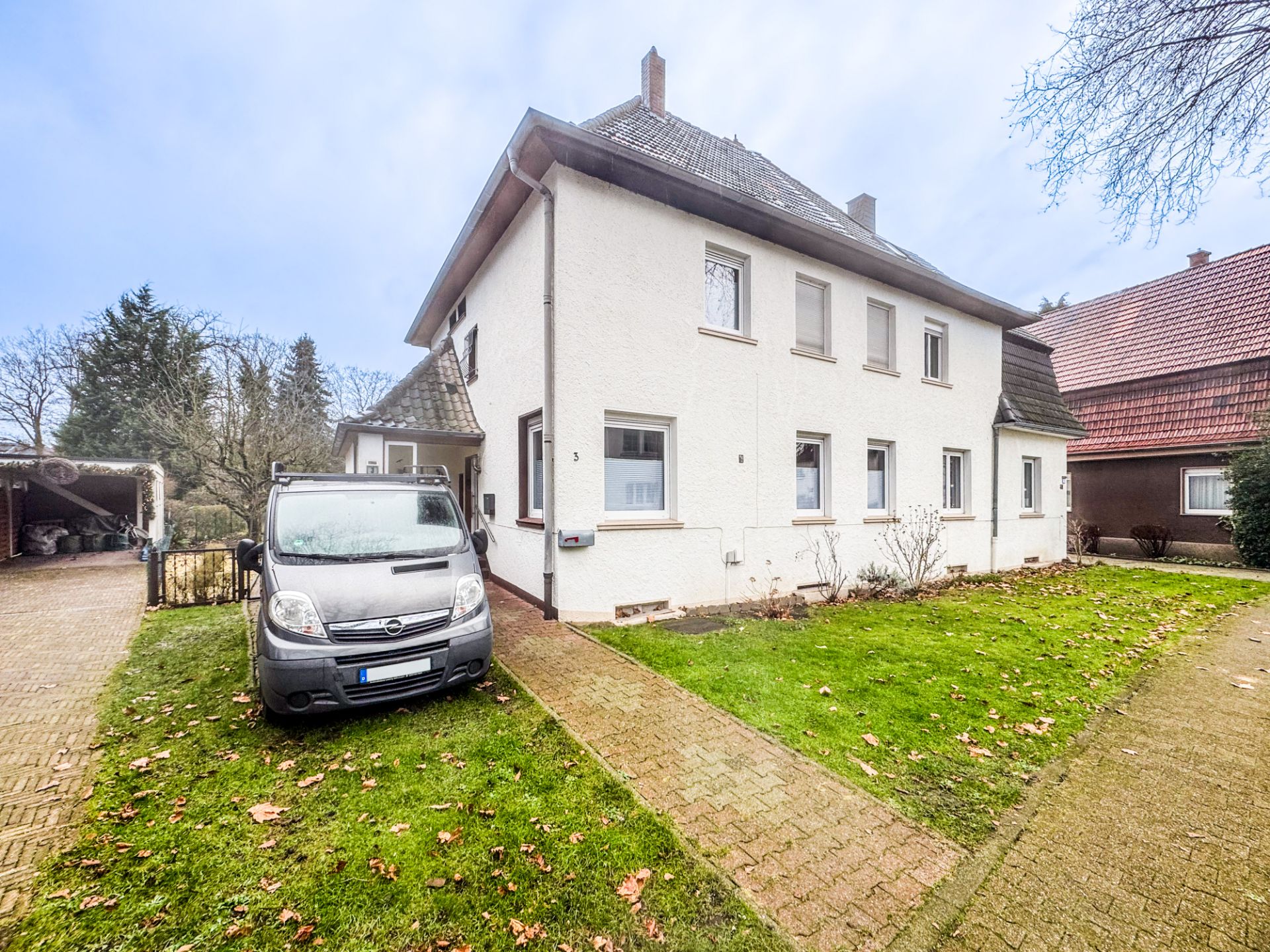 Zweistöckiges Haus mit weißer Fassade, grüner Rasenfläche und geparktem Auto vor dem Eingang.
