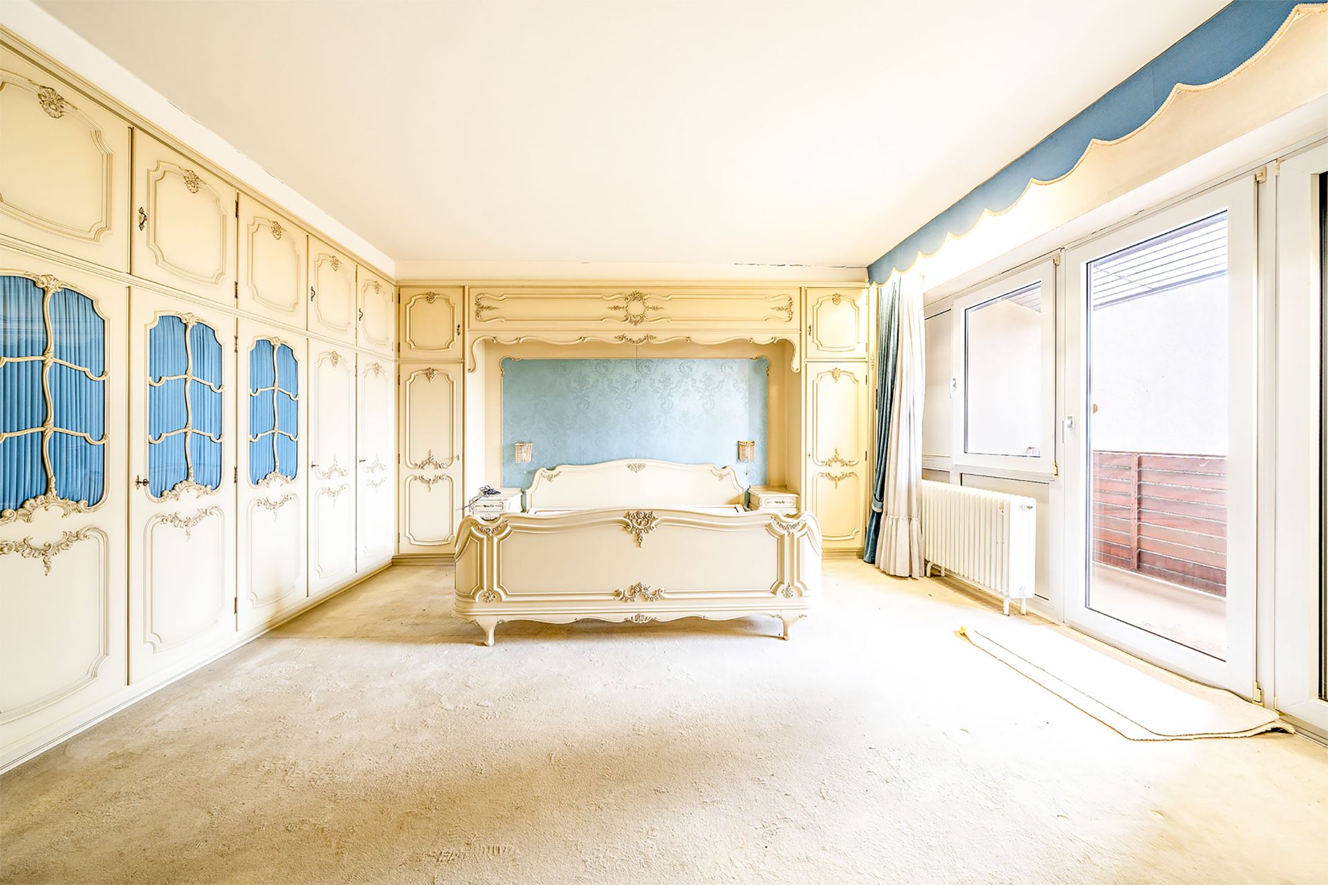Helles Schlafzimmer mit verzierten Einbauschränken, einem Bett und großen Fenstern.
