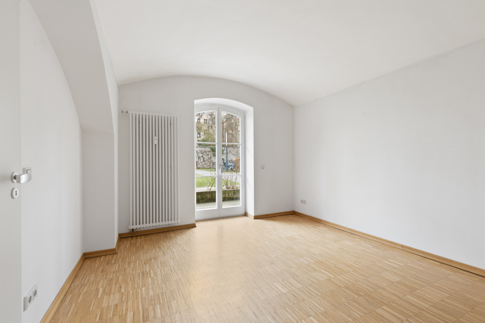 Leerer, heller Raum mit Holzboden, weißem Heizkörper und großer Fenster-Tür.
