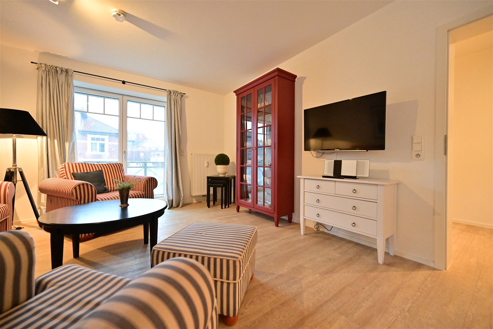 Wohnzimmer mit gestreiften Sesseln, Couchtisch, rotem Schrank und Fernseher an der Wand.