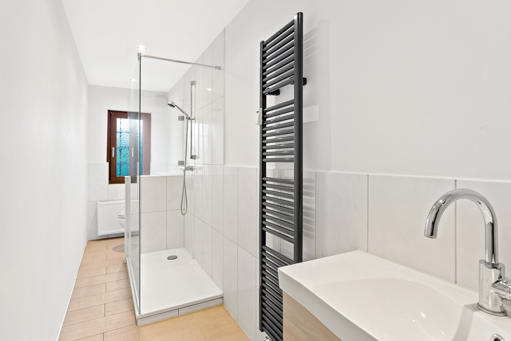 Modernes Bad mit begehbarer Dusche, Waschbecken, Handtuchheizkörper und Fenster.