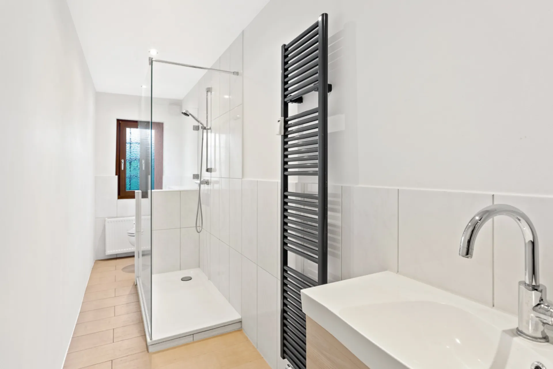 Modernes Bad mit begehbarer Dusche, Waschbecken, Handtuchheizkörper und Fenster.