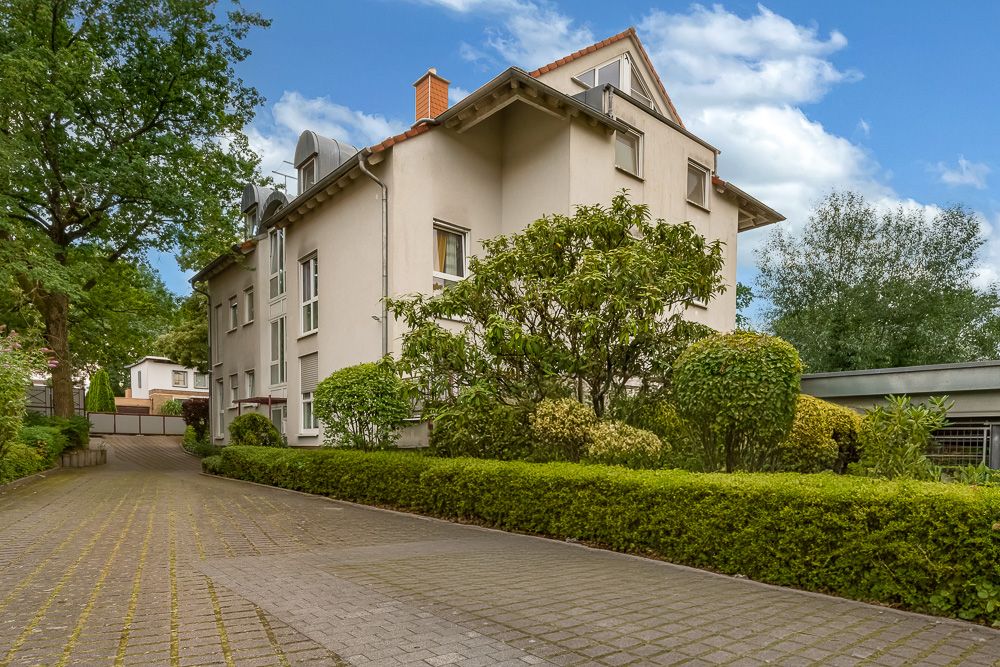 Mehrstöckiges Wohnhaus mit gepflegter Einfahrt, umgeben von Bäumen und Sträuchern.
